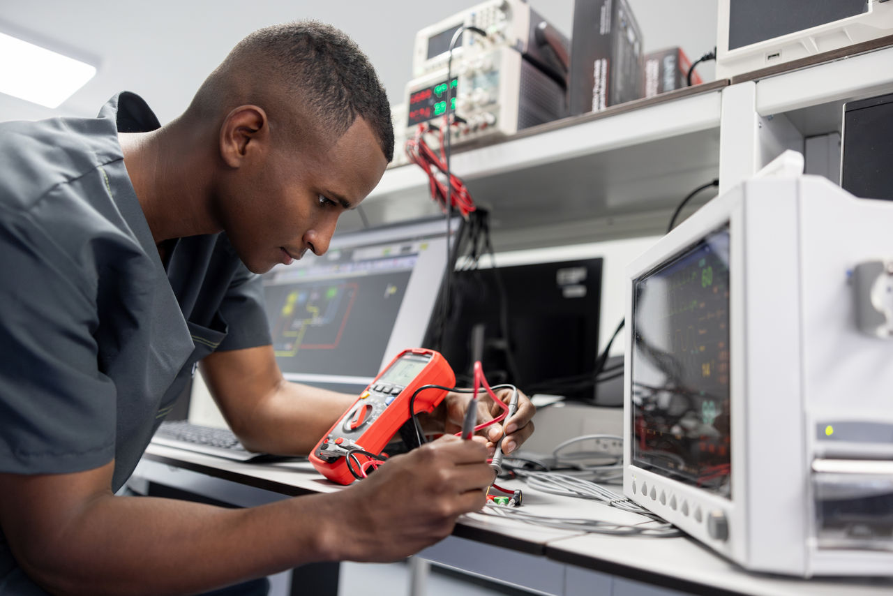 African American electrician repairing medical equipment using a multimeter